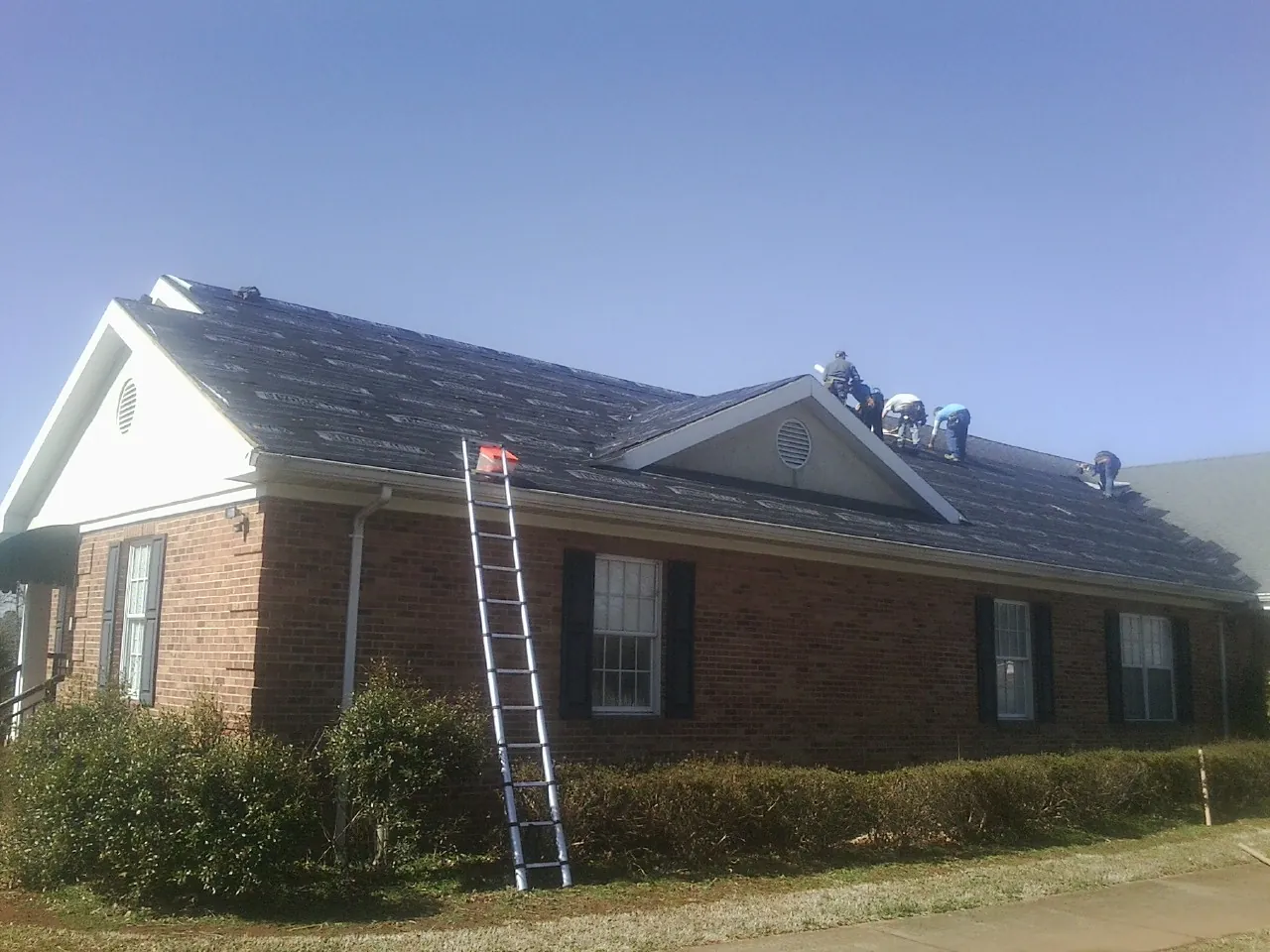 Crew tearing shingles off a brick ranch roof with a ladder set — Metal Roof Repair work by our crew in Mapleton