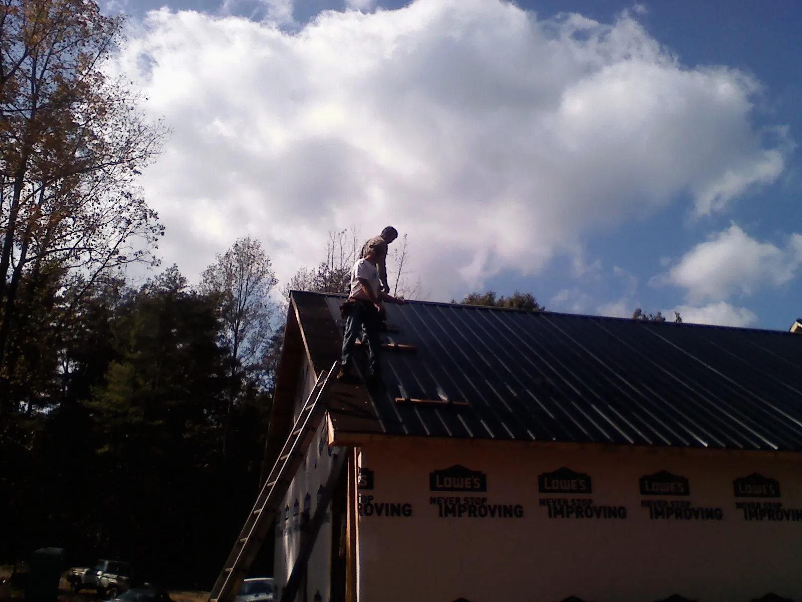 Roofer fastening dark metal panels high against a cloudy sky, from a Roof Inspection job in Mapleton